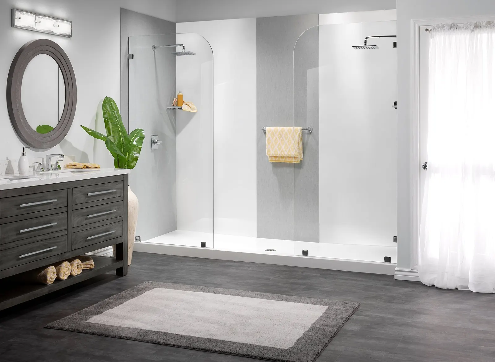 Bright walk-in shower with white and light gray wall panels, a low shower base and clear glass panels, next to a gray wood double vanity